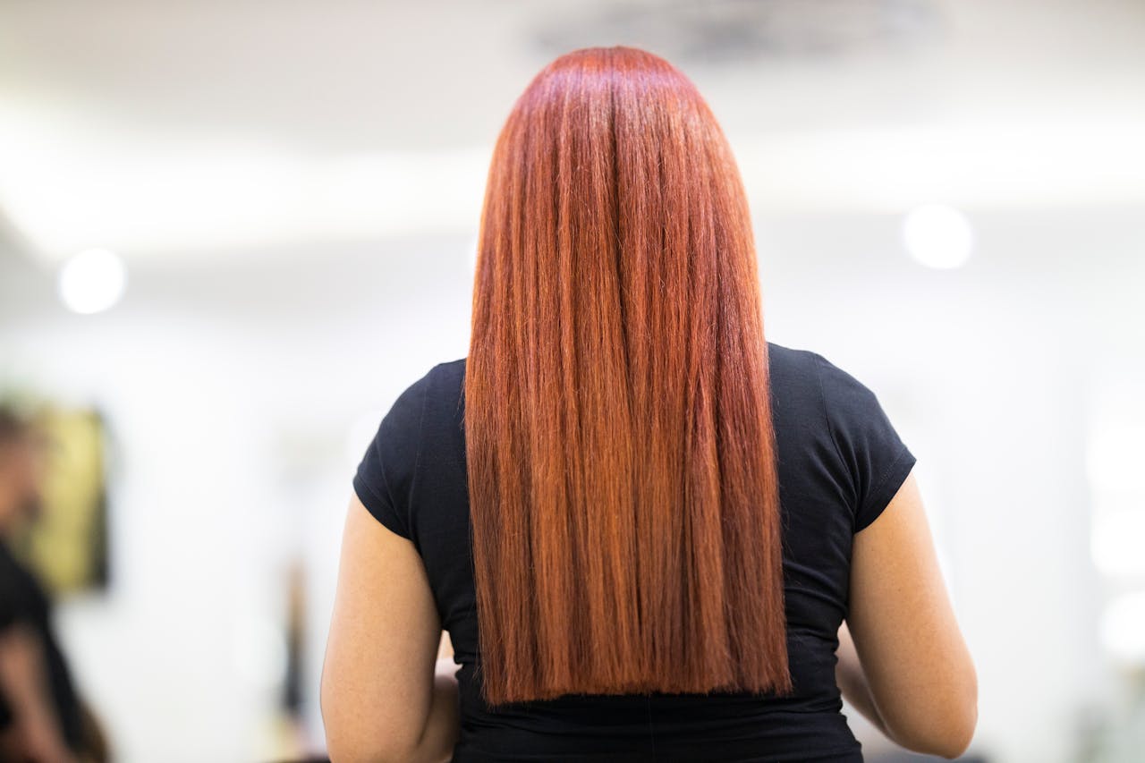 A woman with straight, vibrant red hair seen from the back, showcasing a fresh hairstyle in a professional salon.