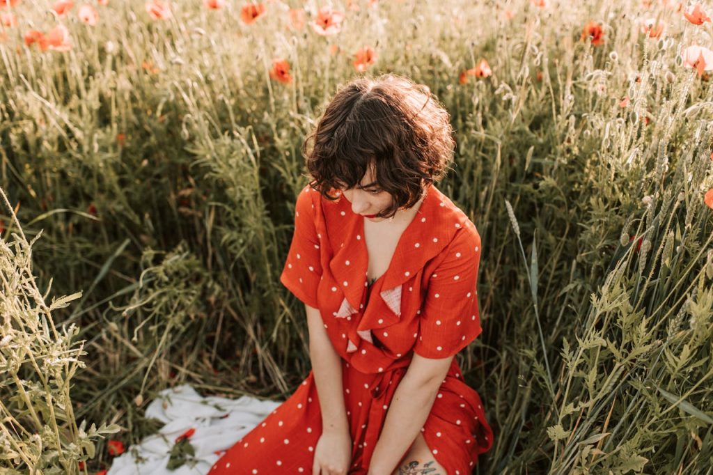 A woman in a red polka dot dress sits thoughtfully in a field of poppies.